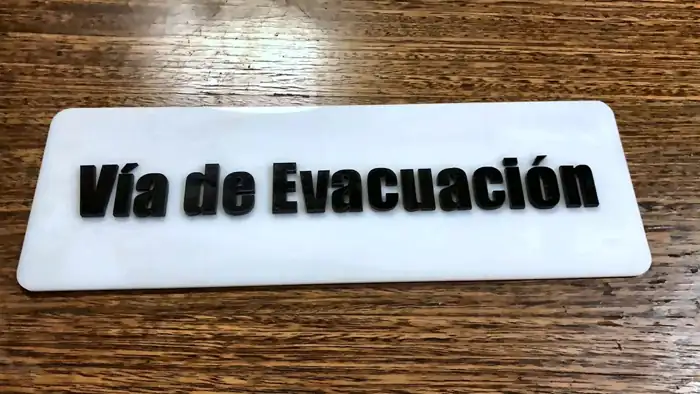 Letrero de acrílico blanco con letras negras Vía de Evacuación